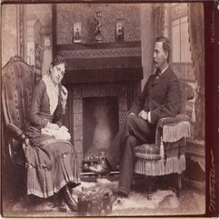 COUPLE SITS IN FRONT OF A FIREPLACE IN COMFORTABLE LIVING ROOM IN - Karbonix